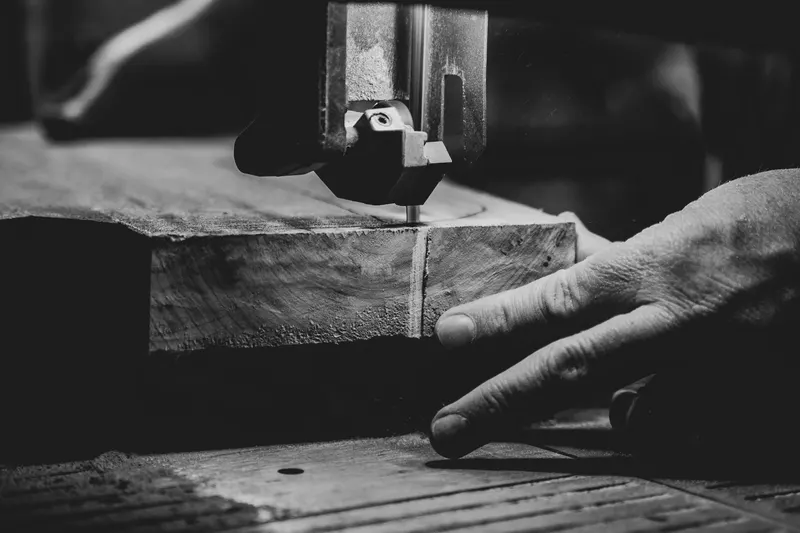 Black and white close-up of hands guiding wood through a saw